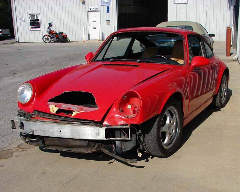Classic vintage red Porsche with a hole in the hood, missing front light, and a bent bumper.