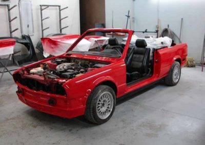 Red 1993 BMW 325i convertible E30 without the hood, doors and windows during repair process.