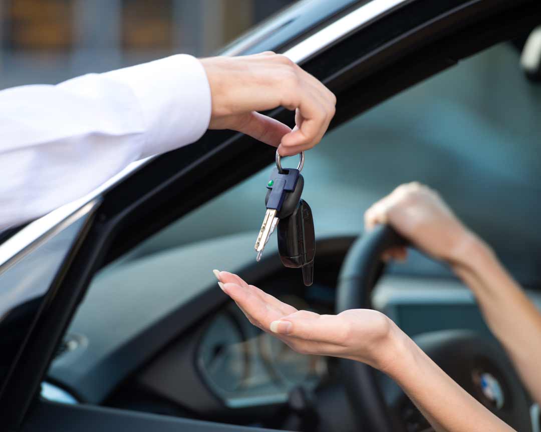 Man handing down keys to a rental car to a woman inside the car.