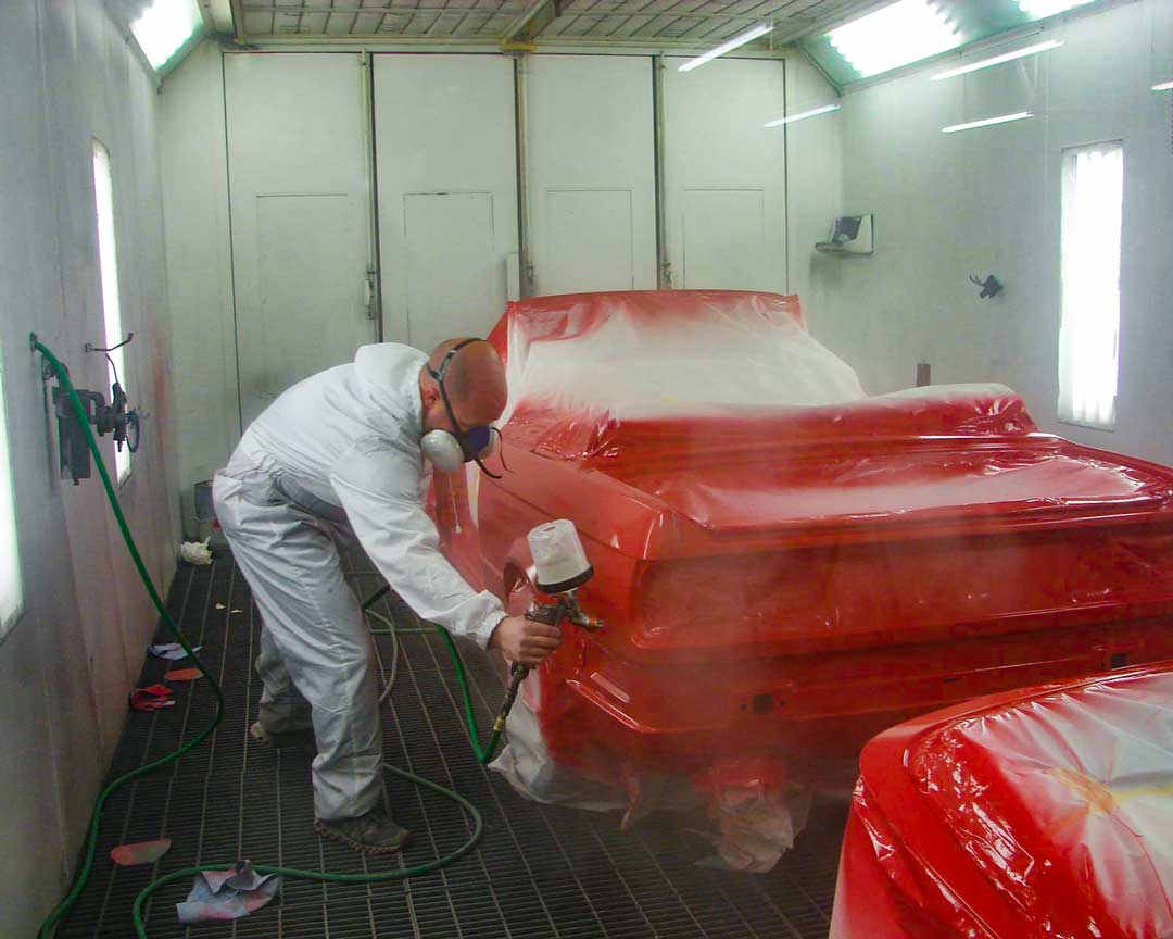 Diamond Collision Services worker repainting a car red with a special tool.